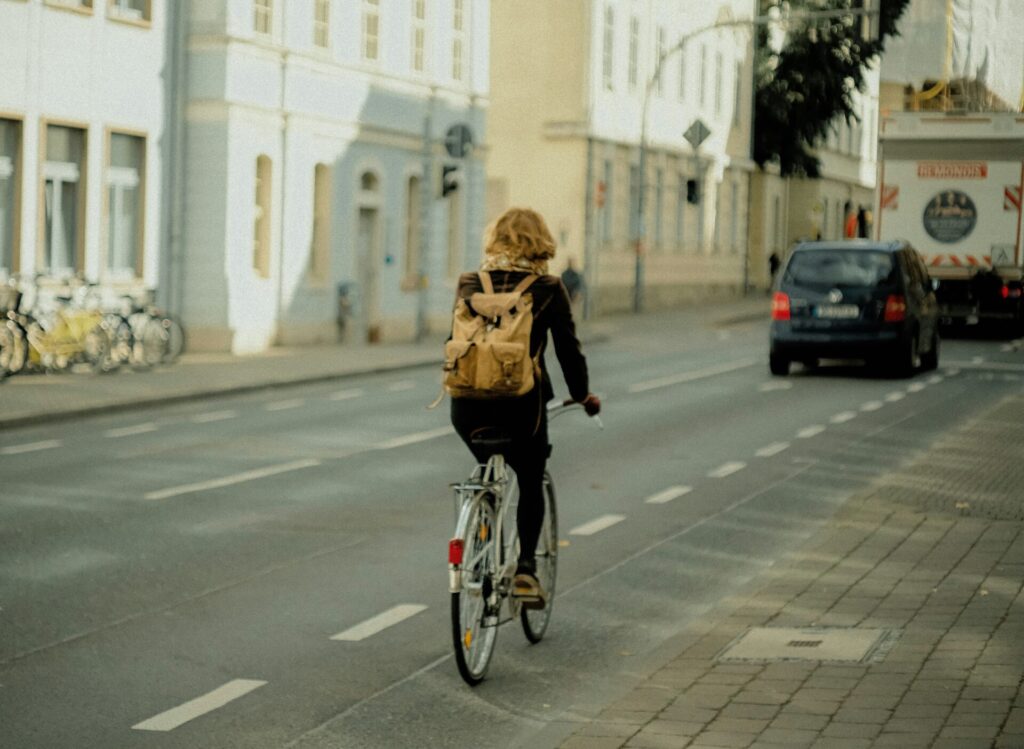 街の中をリックサックを背負った女性が自転車で走っているのを背後から見た画像