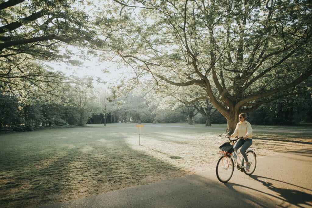 公園の道を女性が自転車に乗って走っている画像